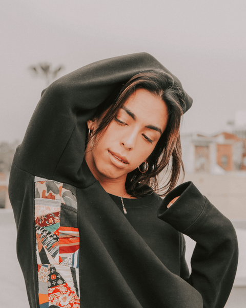 A photo of an androgynous model on a Los Angeles rooftop in a black upcucled sweater with a vintage black and white photo of a Florida man in the background.