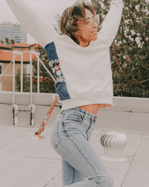 A collage of a non-binary, androgynous model poses in vintage jeans and the bubuleh fenway denim sweater with upcycled jeans and baseball fabric, with drag queens all around and the Yiddish word "Mishegas" along with the words He, She and They.