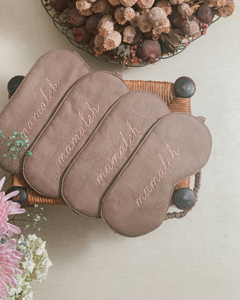 Linen eye masks on a wooden bench with flowers next to them that say mamaleh.