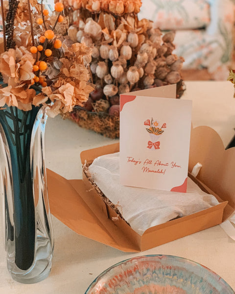 The bubuleh Mother's day gift box opened showing a linen bag, a custom card that says "Today's All About You, Mamaleh" with flowers in the background.