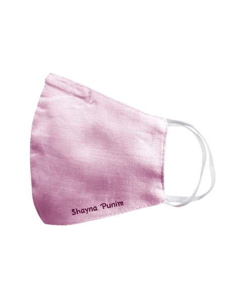 A lilac linen face mask that says shayna punim embroidered in maroon on the bottom left.