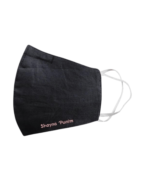 A close up look at the midnight blue spring face mask that says "shayna punim" on each one, with a blurred dark background.