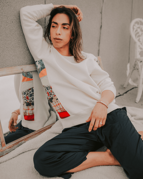 A young androgynous model posing outside next to a wooden french door mirror wearing the bubuleh natural sweet buy psycho sweater.