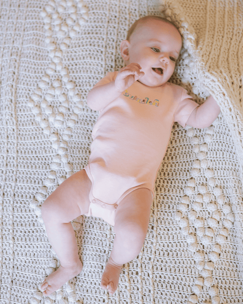 An adorable baby in an orange / apricot-colored onesie with the word "bubuleh" embroidered on the front in six colors.