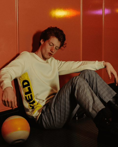 A red haired model spinning a yellow bowling ball at the britely in los angeles while wearing a bubuleh crewneck.