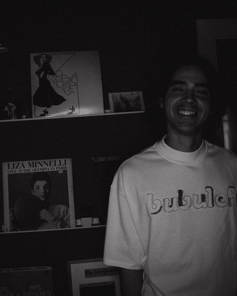 Black and white photo of Jared Goldstein smiling next to a vintage Bette Midler 1970s album