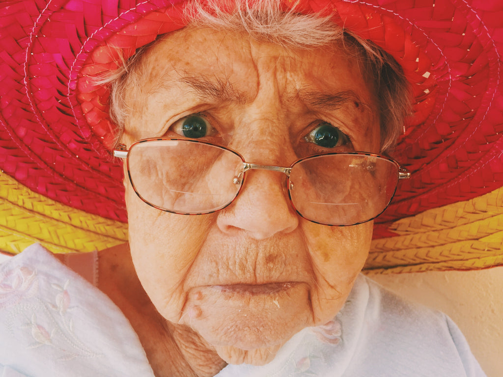 A closeup of an older bubbe / grandma making a concerned face with glasses and a pink hat.