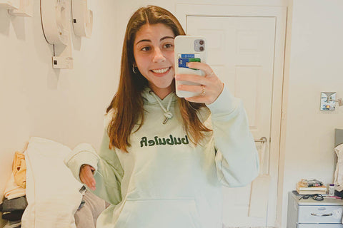 A mirror selfie of a girl in the seafoam bubuleh hoodie smiling in her room.