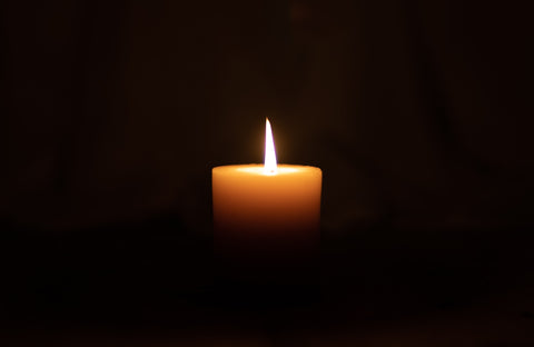 A photo of a lone yellow candle burning amidst blackness all around.