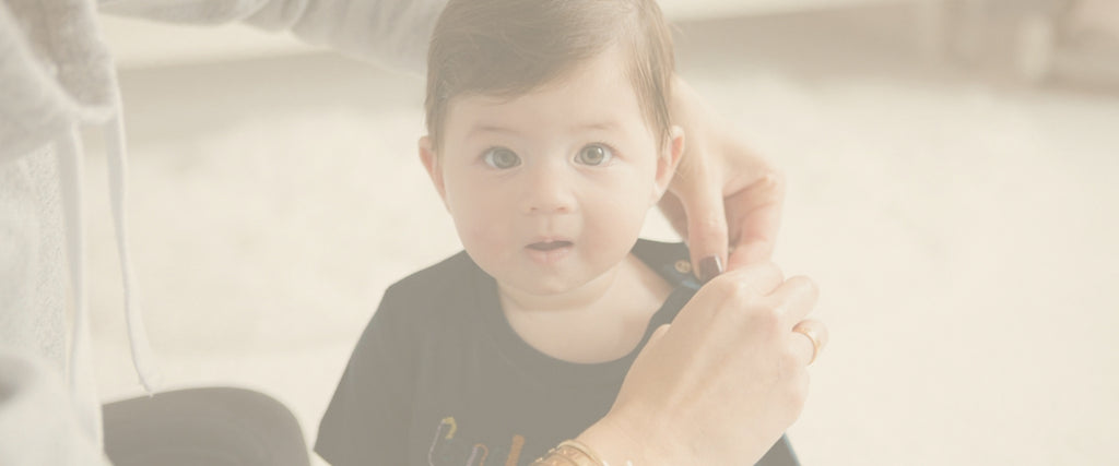A baby girl is being changed into a navy blue shirt by a Mom wearing a cartier love bracelet.
