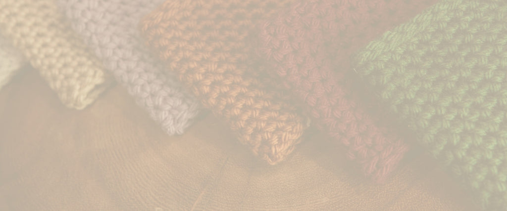 5 colors of crochet coffee cup holders lined up together against a wooden table.