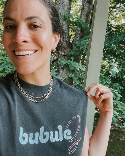 A girl in New York wearing a gold necklace and a black tank top that says "bubulez"