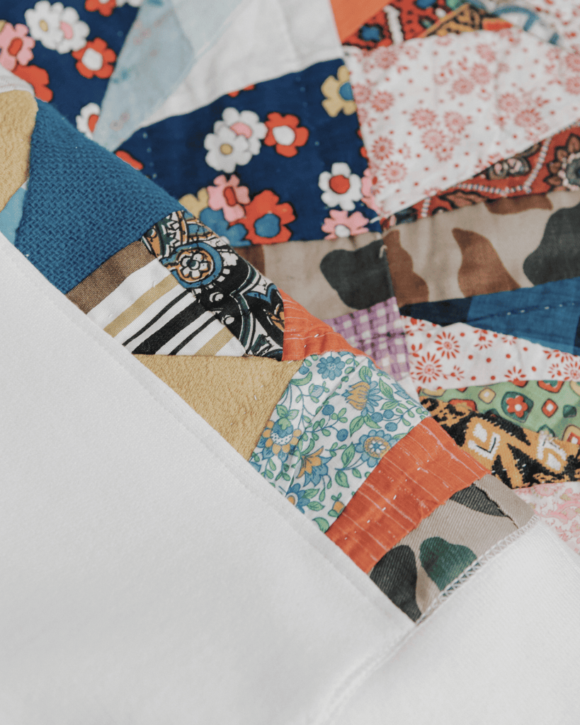 A natural cotton crewneck hanging from a hanger with vibrant orange and blue quilted sides and a quilt on the bottom of the frame.