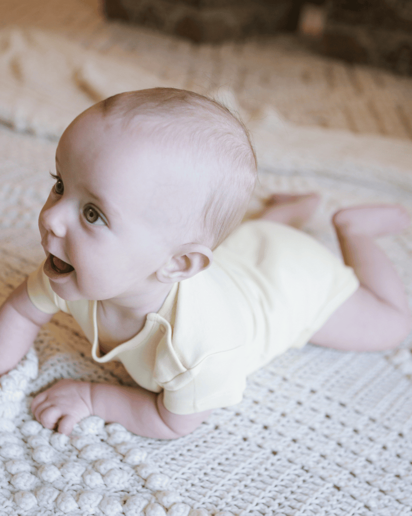 A baby crawling in a yellow bubuleh onesie made with organic cotton in the UK.