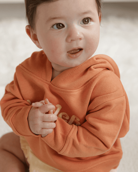 Two side-by-side images of a baby in a pumpkin / orange hoodie smiling.