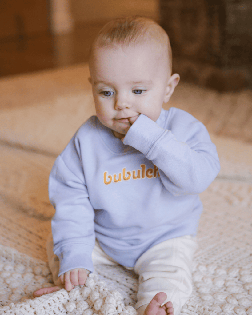 An adorable baby wearing a bubuleh baby blue / blueberry crewneck in organic cotton.