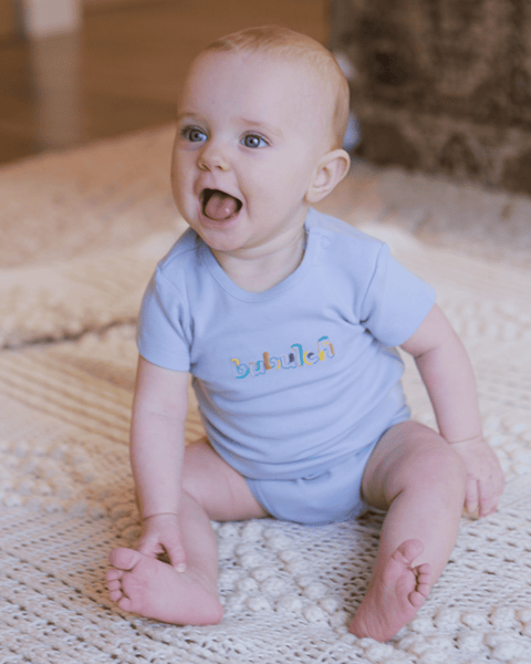 A smiling baby girl with strawberry blonde hair wearing the bubuleh onesie in blueberry.