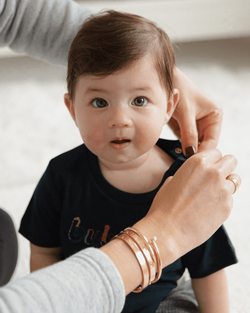 A mom changing her baby while wearing several cartier love bracelets.