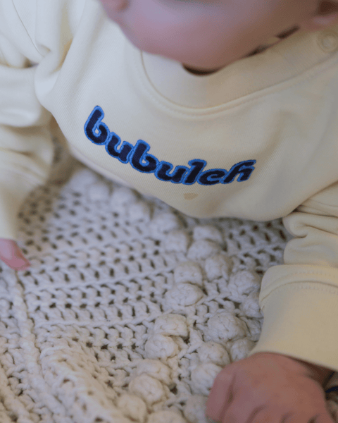 A baby being changed while wearing a butter-colored bubuleh baby mini crewneck.