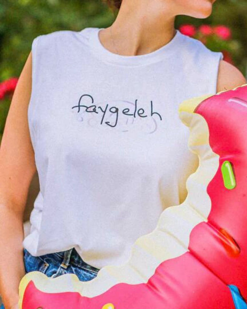 A woman wears the white faygeleh tank top with a donut-inspired pool floatie in her hand.