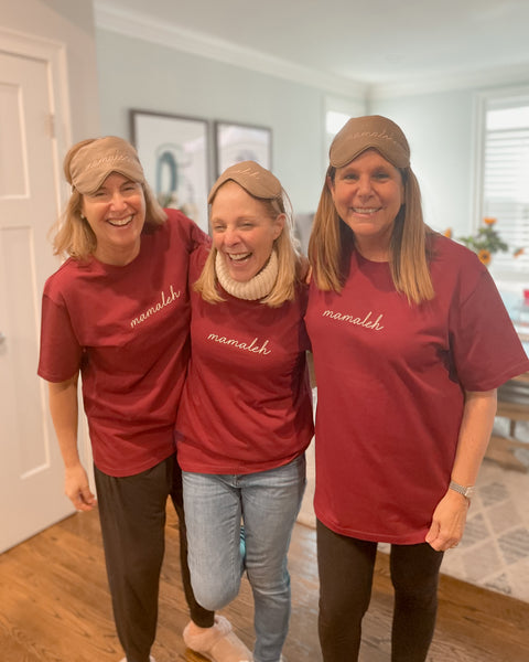 Three mothers smiling in maroon shirts and eye masks that say mamaleh, which is mom in Yiddish.