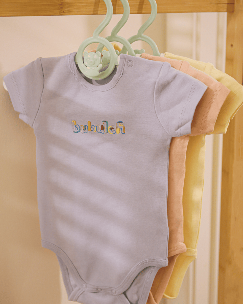 The blueberry baby onesie by bubuleh hanging on a wooden rack.