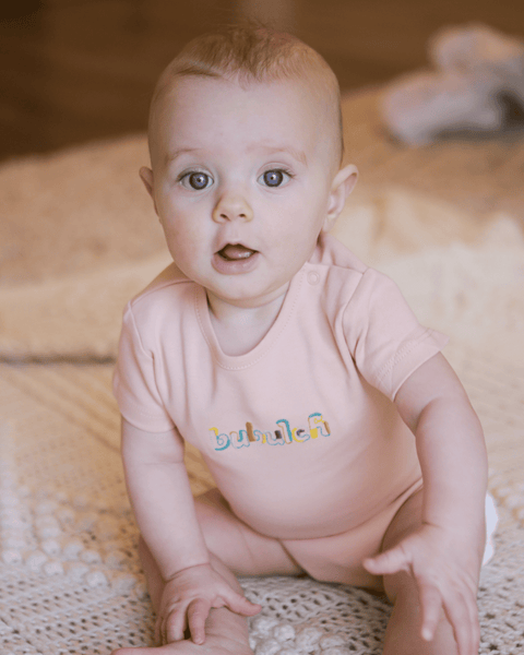A baby smiling in a peach / apricot colored onesie by bubuleh with unique embroidery