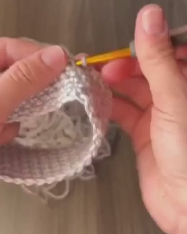 A video of someone crocheting a heather gray coffee sleeve at home on a gray table.