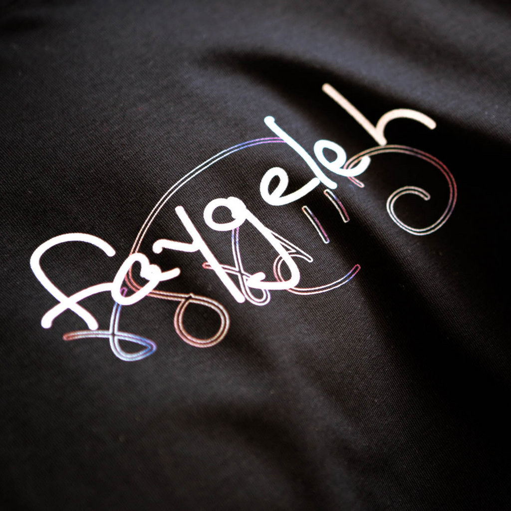 A closeup shot showing the words faygeleh in Hebrew and in English printing on a black, supima cotton shirt.