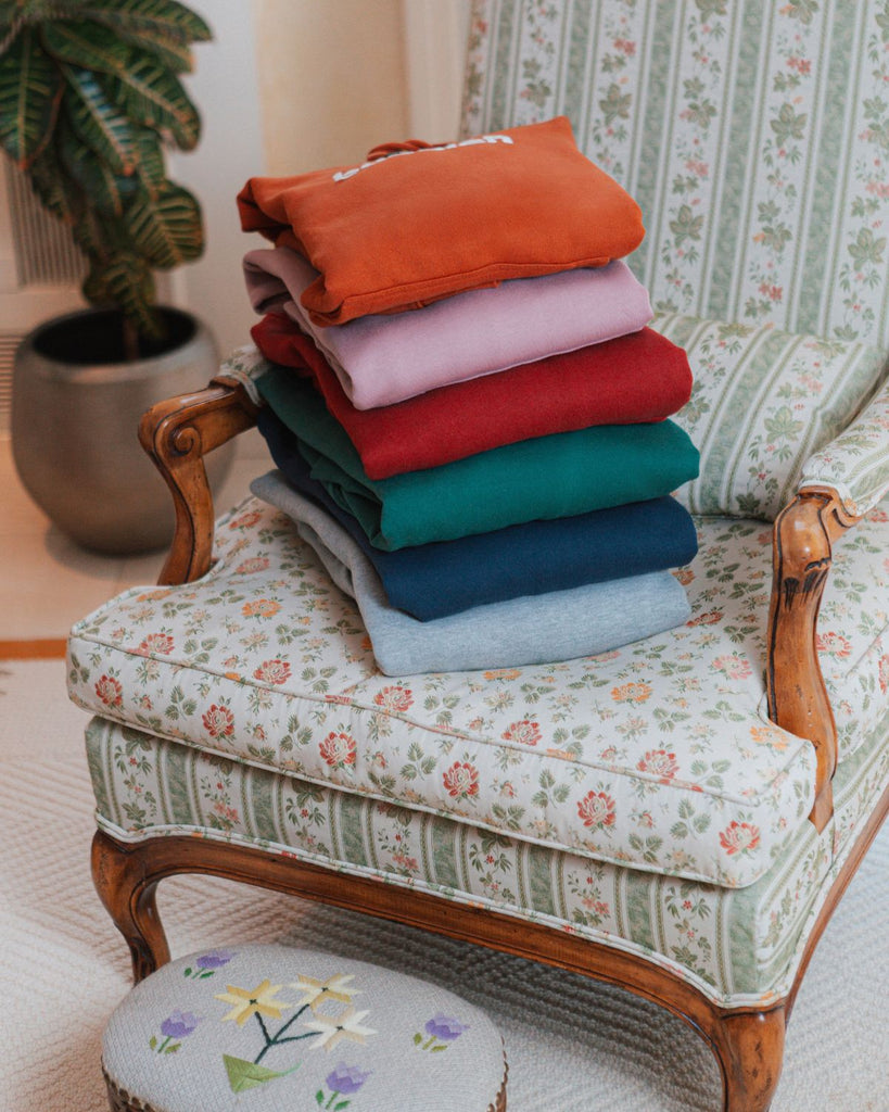 A styled pile of bubuleh sweatshirts in six colors on a grandma's vintage flower couch.
