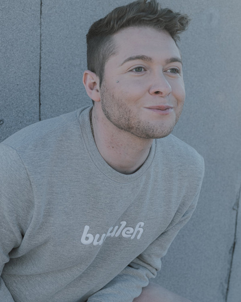 bubuleh founder and CEO Jordan Star smiles off camera in a bubuleh heather gray crewneck, handmade and sweatshop-free.