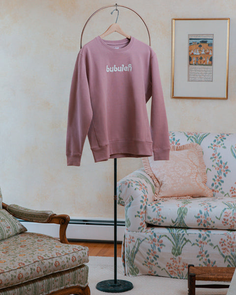 A handcrafted lavender crewneck on a circular valet stand in a bubbe / grandma's living room.