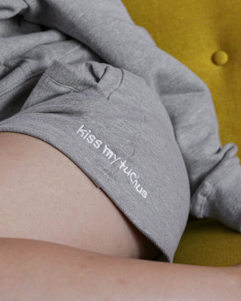 A closeup photo of organic cotton sweatshorts that have the words" kiss my tuchus" embroidered on the sides.