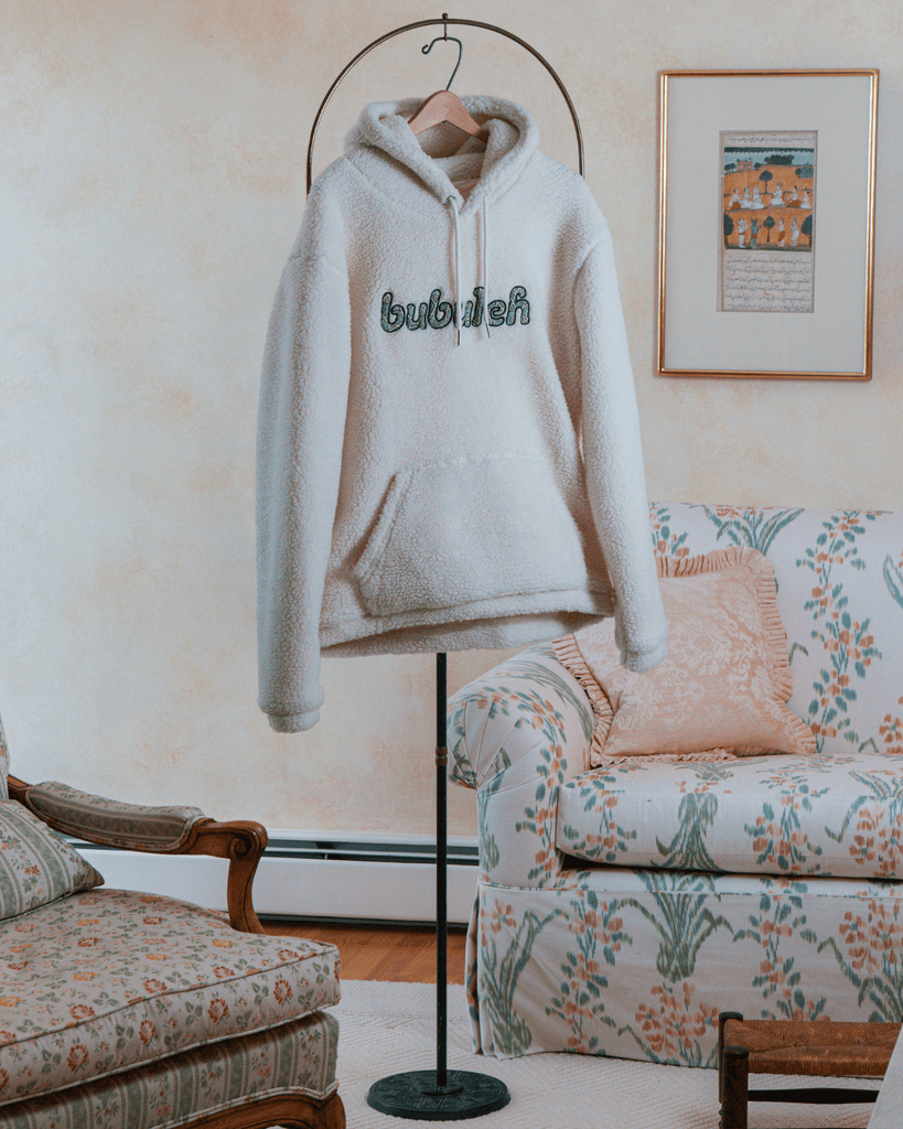 A sherpa hoodie on a clothing stand in a grandma's living room. On the hoodie it says "bubuleh" embroidered on the front