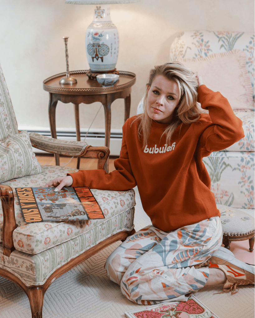 A blonde woman goes through vintage vinyl albums while smiling off camera in a full bubuleh outfit.