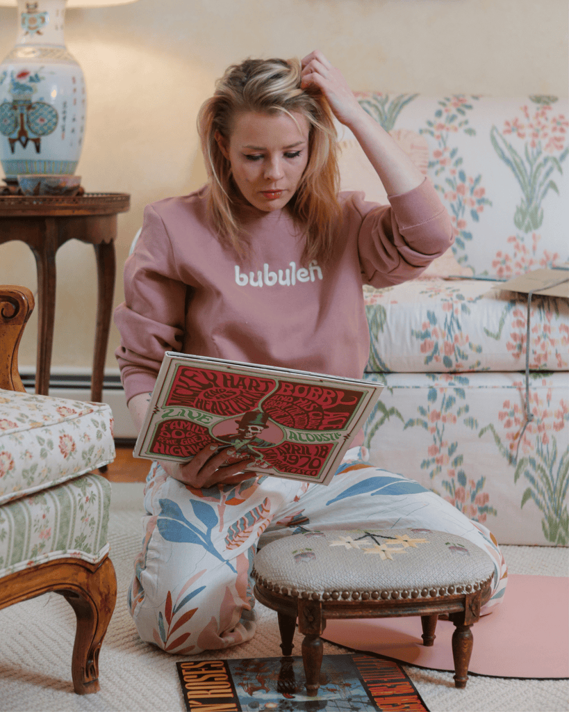 A blonde model looks at an old vinyl album with her hand in her hair while wearing a bubuleh crewneck.