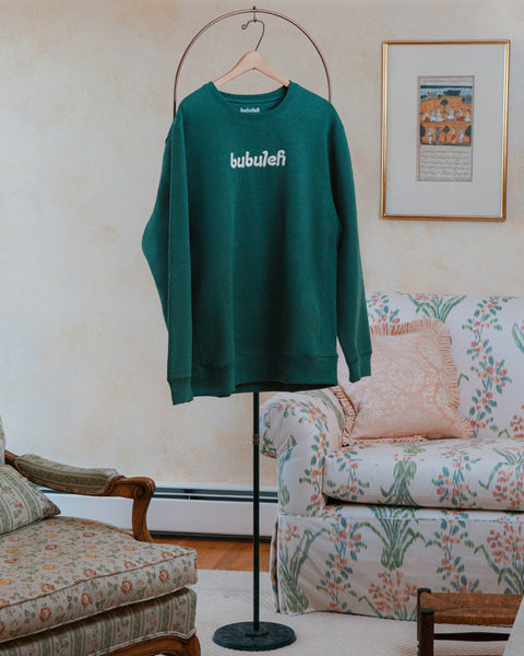 A handcrafted evergreen crewneck on a circular valet stand in a bubbe / grandma's living room.